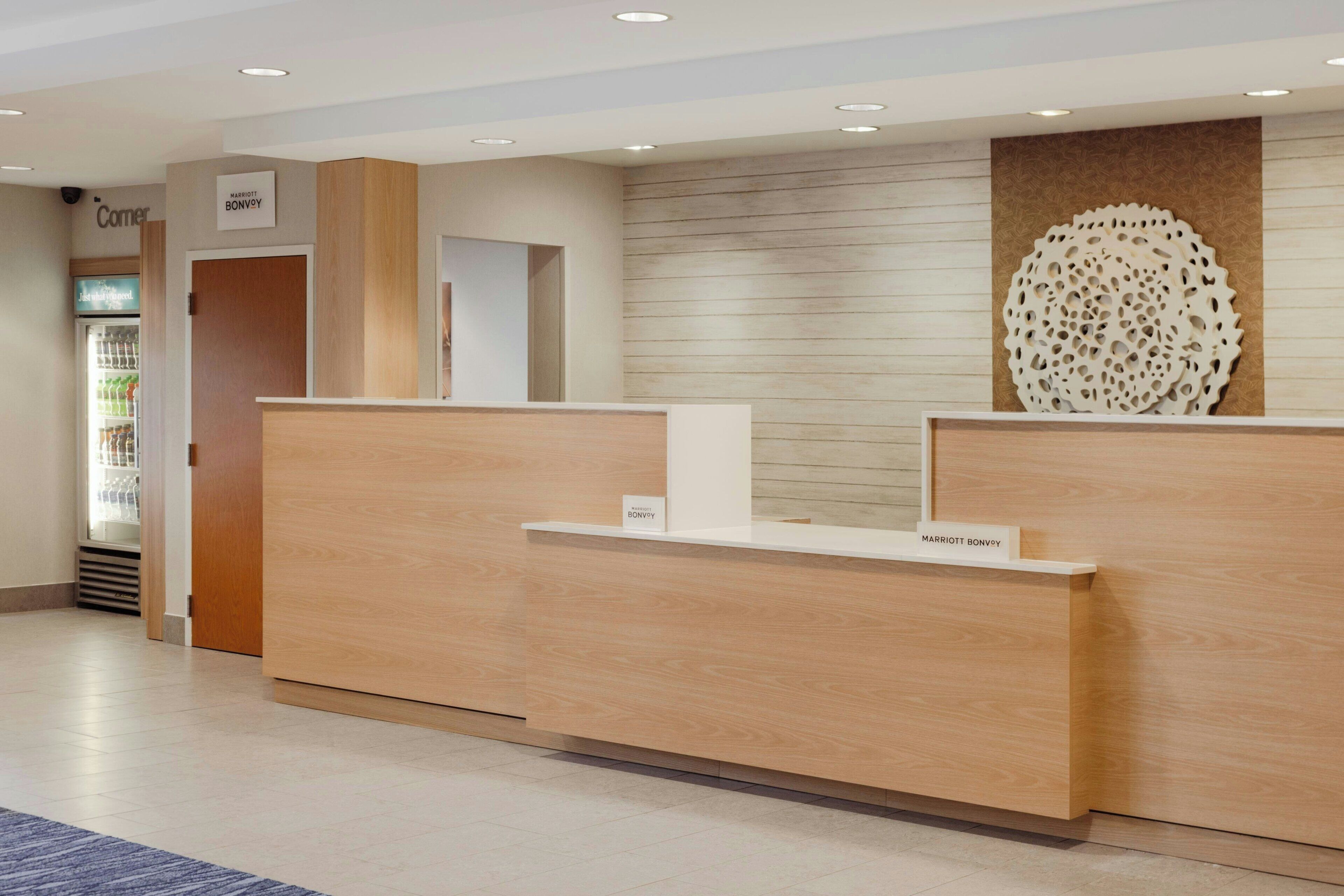 A hotel reception desk with a wooden finish, a sign above it, and a decorative wall piece.