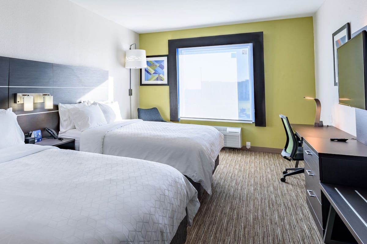 Quarto de hotel com duas camas, uma escrivaninha com computador, televisão e janela com vista.