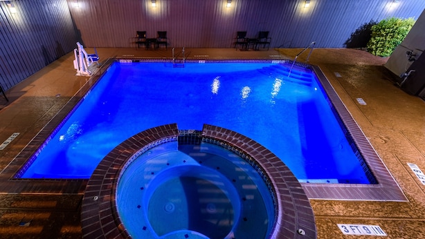 A rectangular swimming pool with a hot tub in the center, surrounded by a brick deck and a wooden wall. - Holiday Inn Express Hotel & Suites Bastrop by IHG (Bastrop)