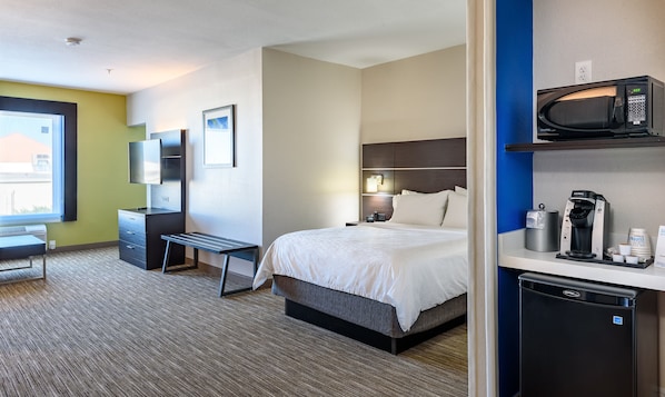 A hotel room with a bed, bedside table, desk, chair, TV, and a coffee machine. - Holiday Inn Express Hotel & Suites Bastrop by IHG (Bastrop)