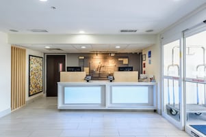 Una recepción de hotel con un quiosco de registro digital, una obra de arte enmarcada en la pared y una entrada por puerta de vidrio.