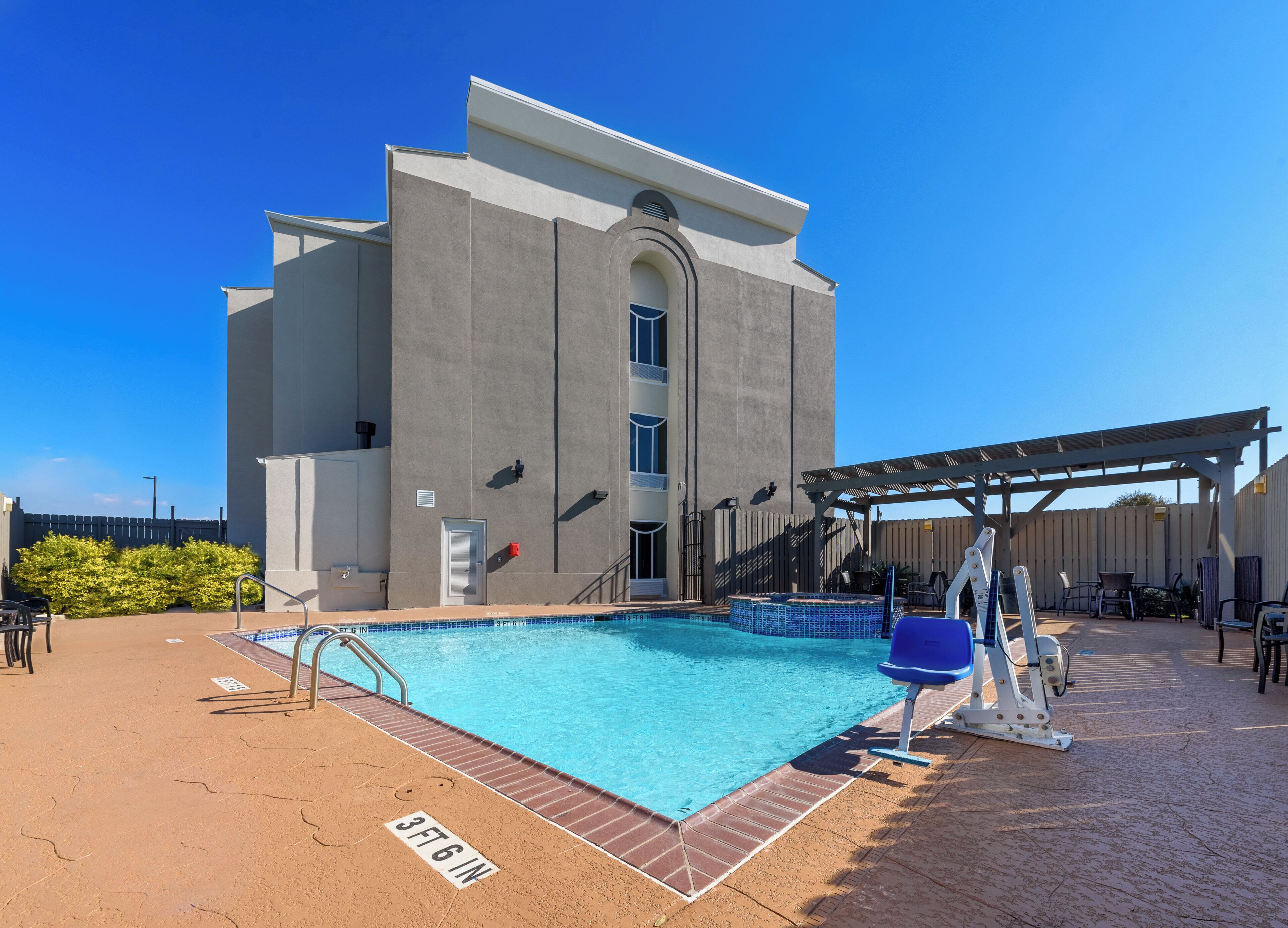 Una piscina con indicador de profundidad de 1 metro 18 centímetros, un área de estar techada y un edificio de diseño moderno.