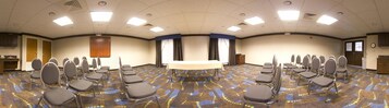 Un salón de conferencias con una larga mesa, varias sillas y piso alfombrado.