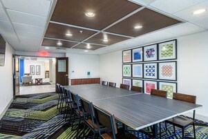 Un salón de conferencias con una mesa larga, sillas y una alfombra estampada.