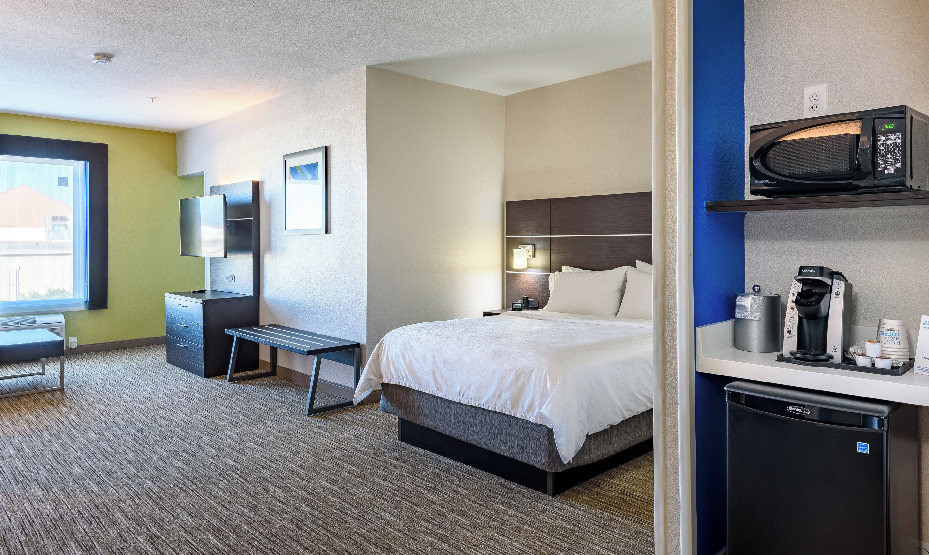 A hotel room with a bed, bedside table, desk, chair, television, and a coffee machine.