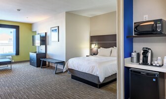 Habitación de hotel con cama, mesita de noche, escritorio, silla, televisión y cafetera.