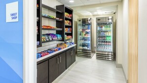 A hallway with a snack display and two refrigerated beverage dispensers. - Holiday Inn Express Hotel & Suites Bastrop by IHG (Bastrop)