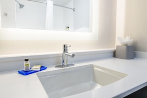 A bathroom with a white sink, a mirror, and a towel dispenser. - Holiday Inn Express Hotel & Suites Bastrop by IHG (Bastrop)
