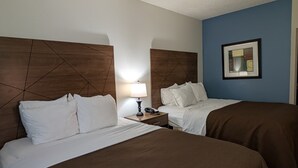 A hotel room with two beds, a nightstand with a lamp, and a framed picture on the wall.