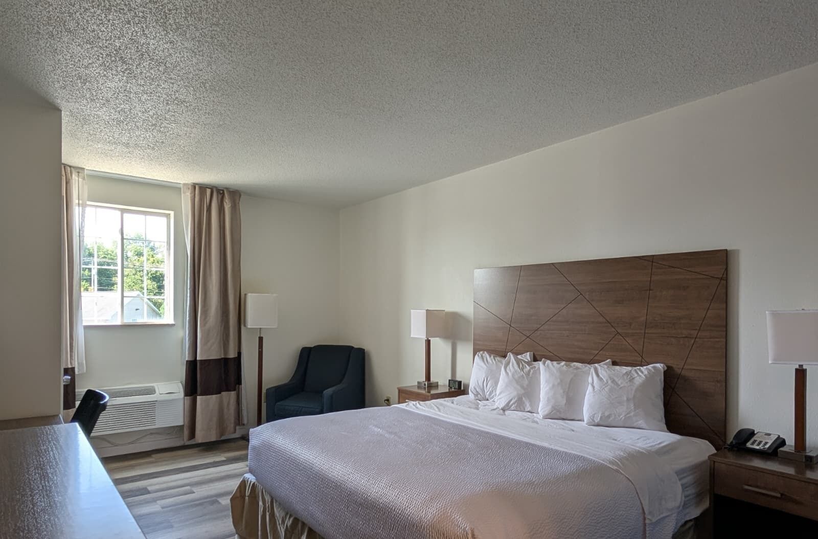 Een hotelkamer met een bed, een stoel, een bureau en een raam met gordijnen.