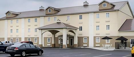 A multi-story hotel with a central entrance, parking lot, and outdoor seating area.
