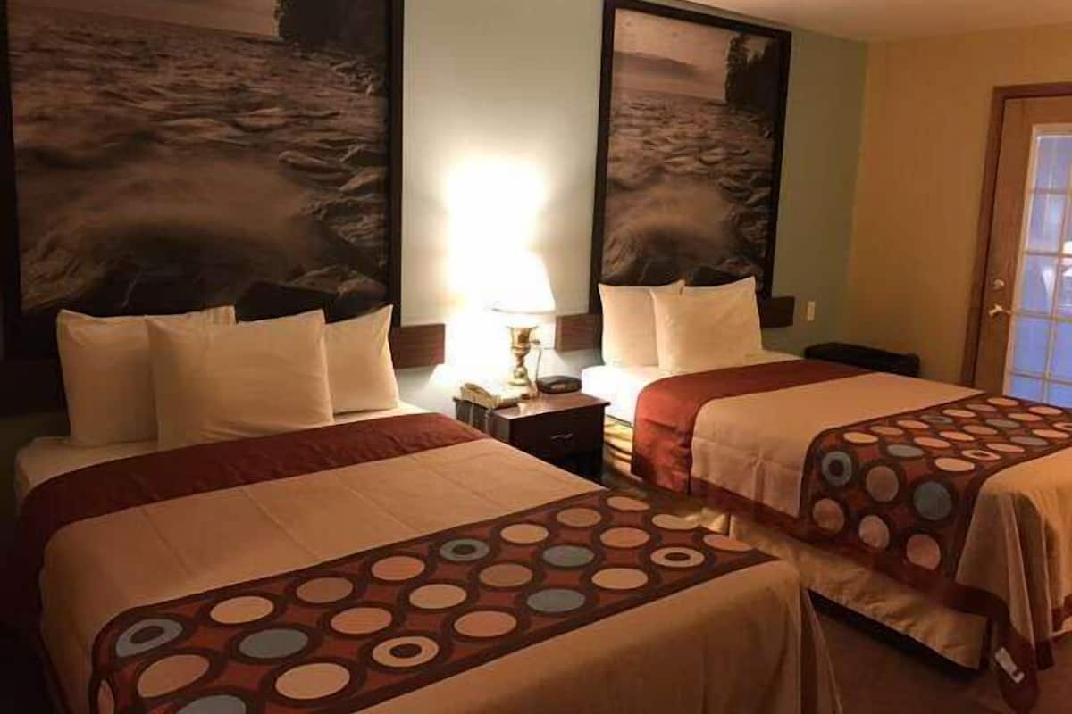 Hotelkamer met twee bedden, elk voorzien van een gebedekt sprei en kussens. Twee grote landschapsschilderijen hangen aan de muren, een nachtkastje met een lamp, en een deur met een geëtste ruit.