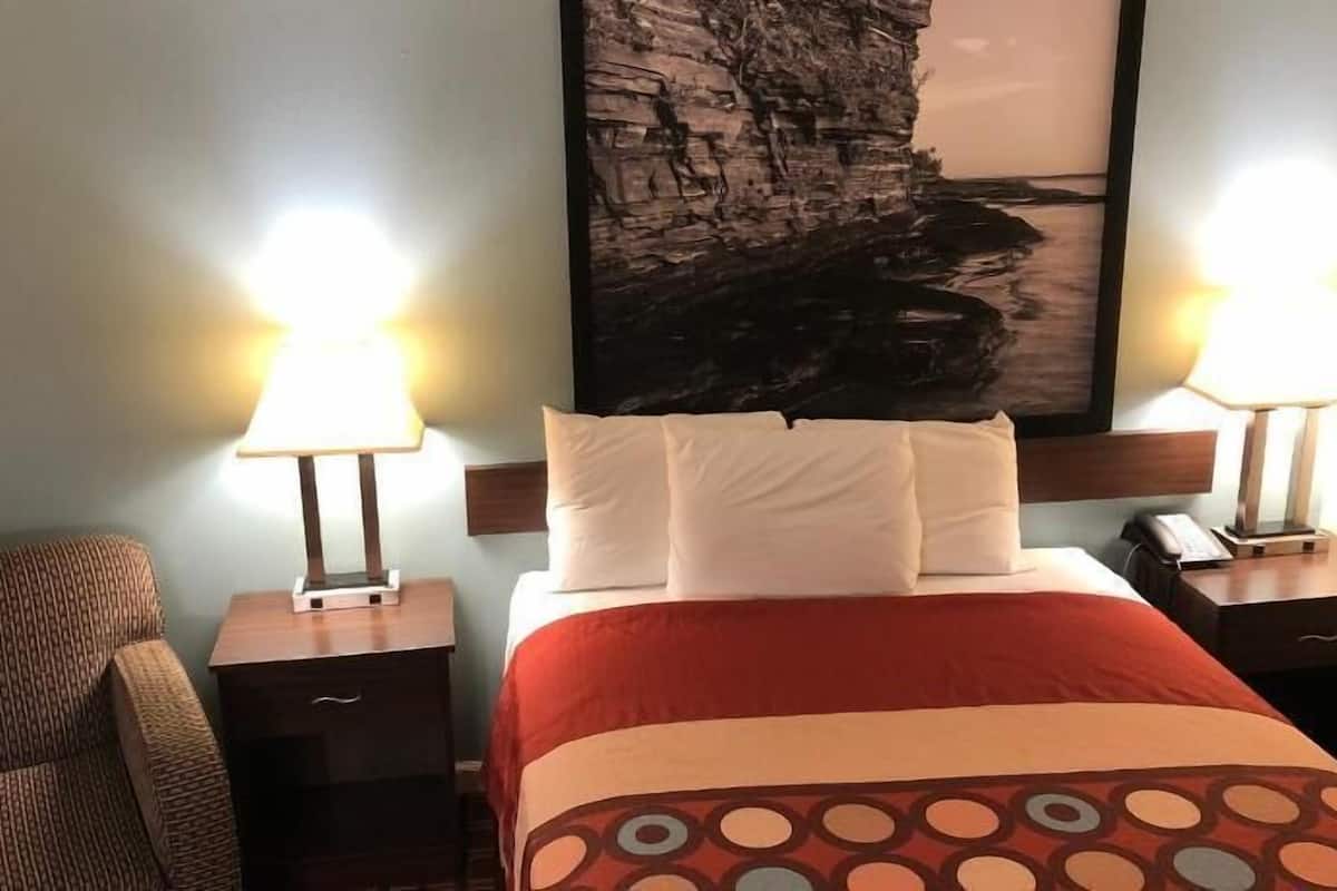 Een hotelkamer met een bed, twee bedlampjes, een stoel, een groot abstract schilderij aan de muur en een nachtkastje met een telefoon.