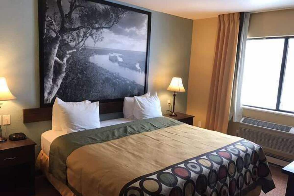 Een hotelkamer met een groot bed, twee nachtkastjes met lampen, een groot fotokader aan de muur en een raam met gordijnen.