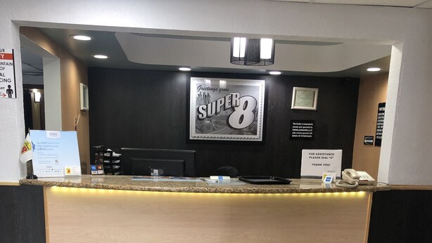 A hotel reception desk with a 'Super 8' sign above it, a phone, and a 'For Assistance' sign.