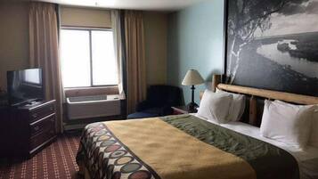 A hotel room with a bed, a television, a desk, a lamp, and a painting of a landscape.