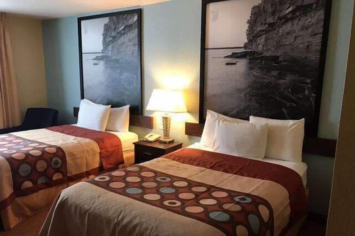 Een hotelkamer met twee bedden, een nachtkastje met een lamp en een schilderij van een kustlandschap.