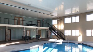 An indoor swimming pool with a clear view of the pool area, a staircase leading to an upper level, and a balcony with outdoor seating.