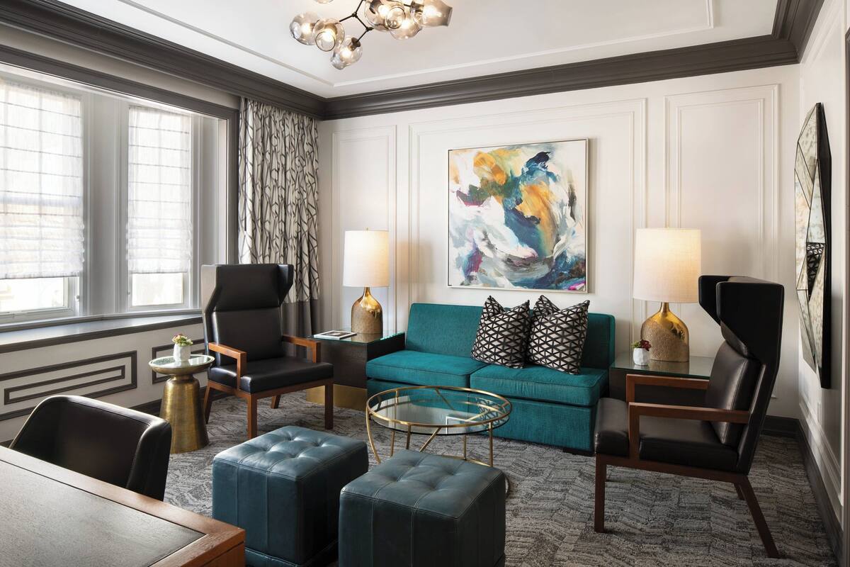 Un salon moderne avec un canapé de couleur turquoise, des fauteuils en cuir noir, une table basse en verre et un grand tableau abstrait accroché au mur.