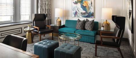 A modern living room with a teal sofa, black leather chairs, a glass coffee table, and a large abstract painting on the wall.
