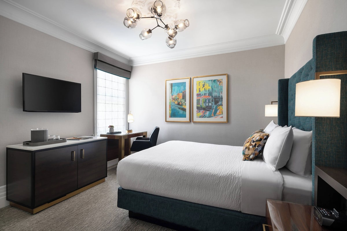Une chambre d’hôtel avec un lit, un bureau, une télévision et des œuvres d’art accrochées au mur.