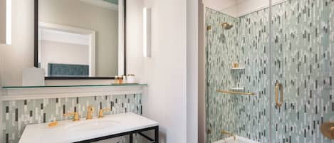 A bathroom with a white sink, a large mirror, and a shower with a mosaic tile wall.