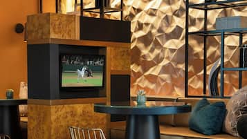 A modern bar area with a television mounted on a wooden pillar, a bar stool, and a seating area with a cushioned bench and pillows.