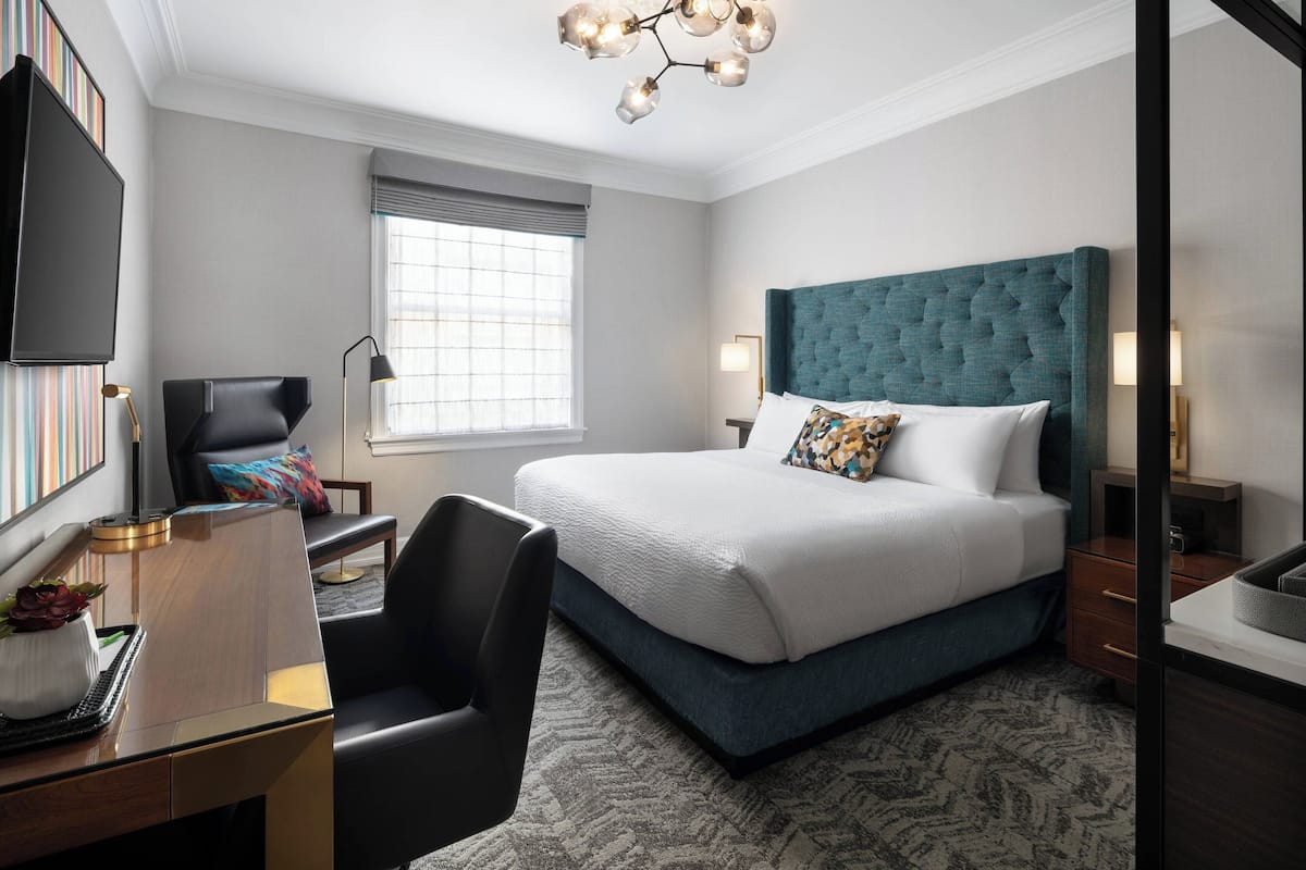 Une chambre d’hôtel moderne, dotée d’un grand lit, d’un bureau avec une chaise, d’une télévision et d’une fenêtre avec des stores.