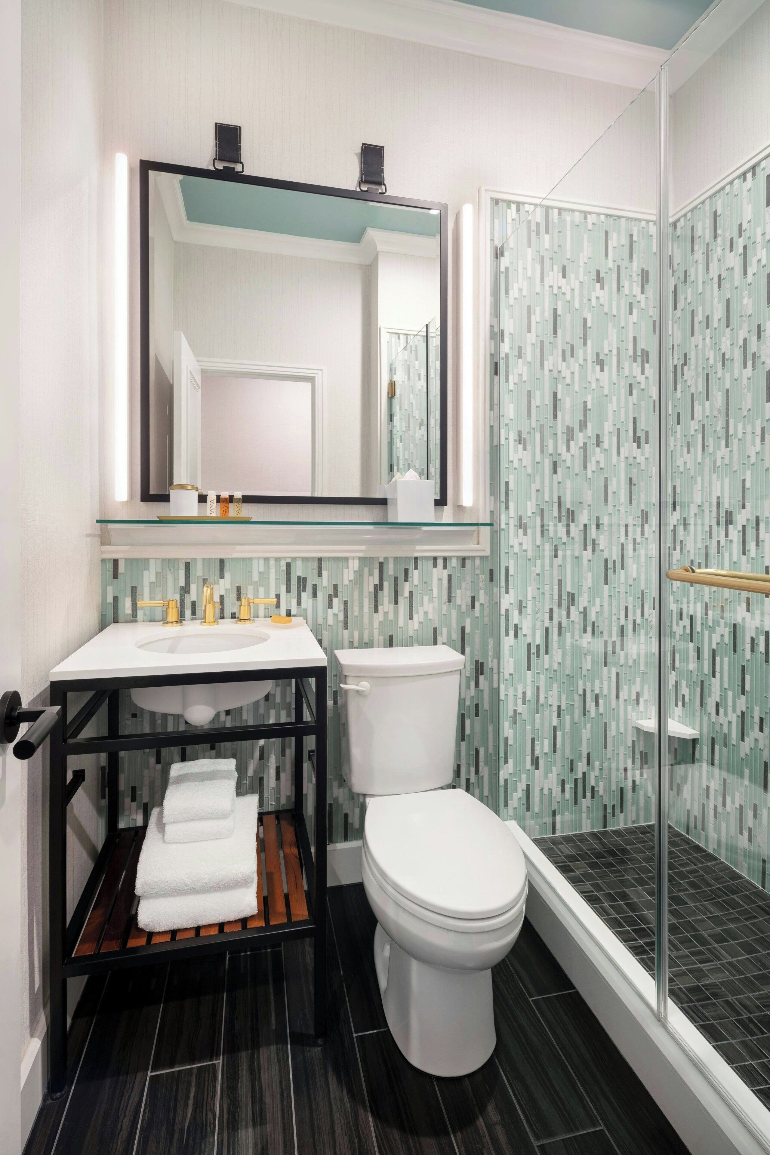Un baño moderno con cabina de ducha de vidrio, inodoro blanco y tocador con estante de cristal.