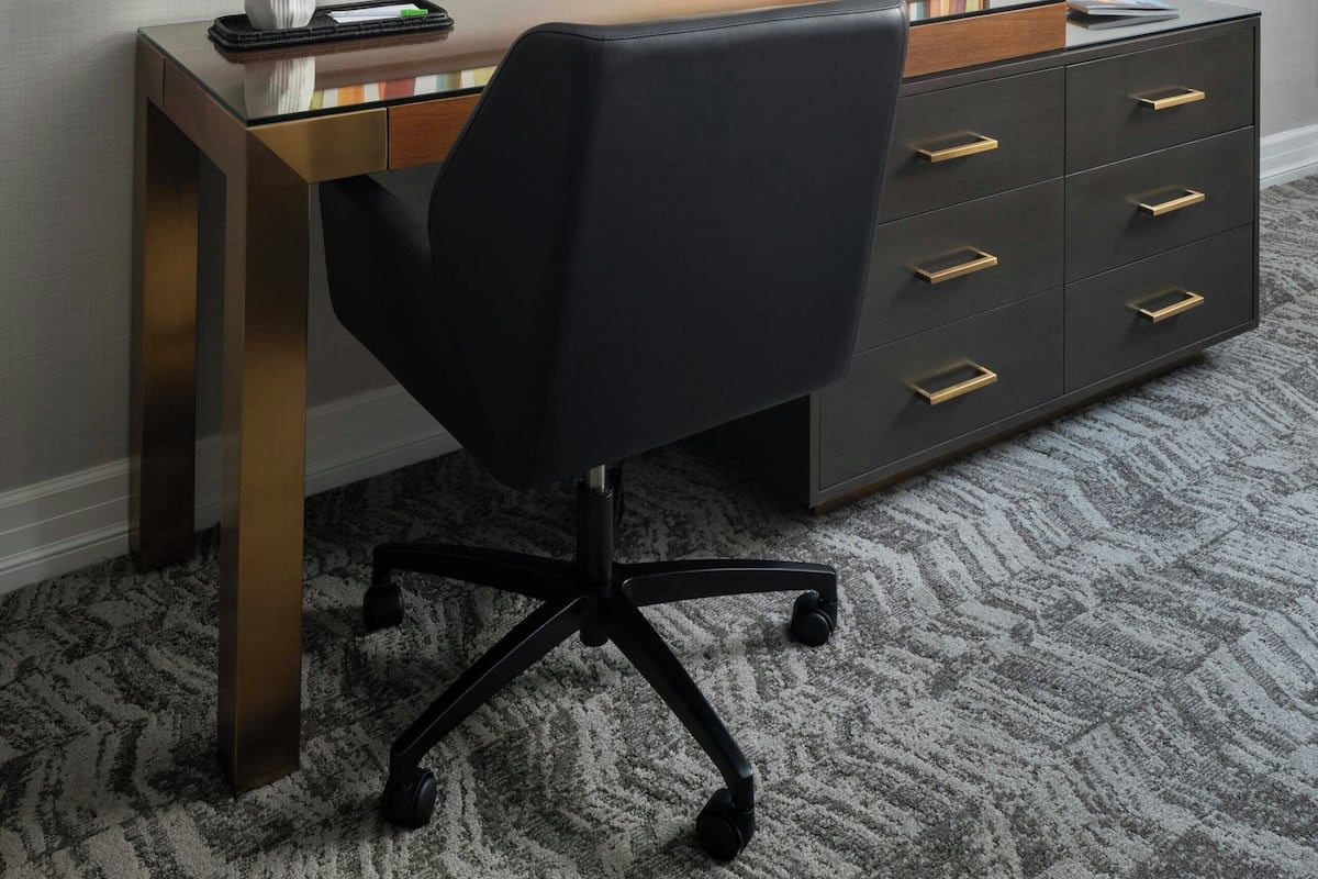 Une chambre d’hôtel moderne équipée d’un bureau, d’un fauteuil de bureau noir, d’un téléviseur à écran plat fixé au mur et d’un élément décoratif mural.