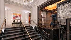 Een statige trap met zwart tapijt en gouden balustrades, die uitkomt op een houten plateau.