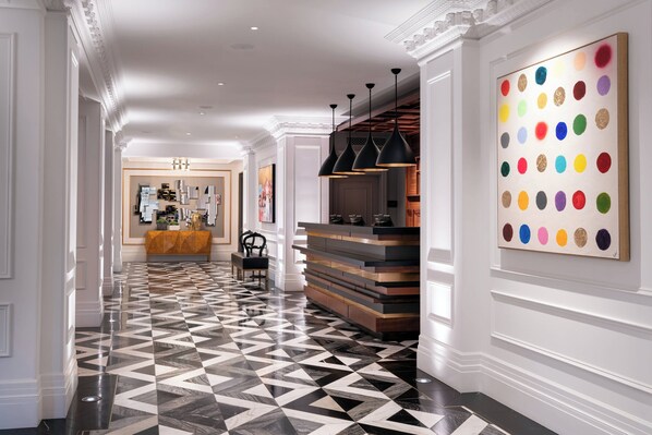 Un vestíbulo de hotel con suelo de diseño geométrico, un mostrador de recepción y una obra de arte colorida en la pared.