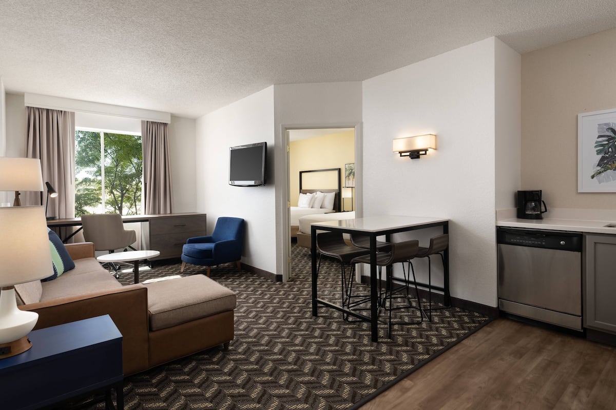 Une chambre d’hôtel équipée d’un canapé, d’un fauteuil, d’une table à manger, de chaises, d’une télévision, d’une machine à café et d’un lave-vaisselle.