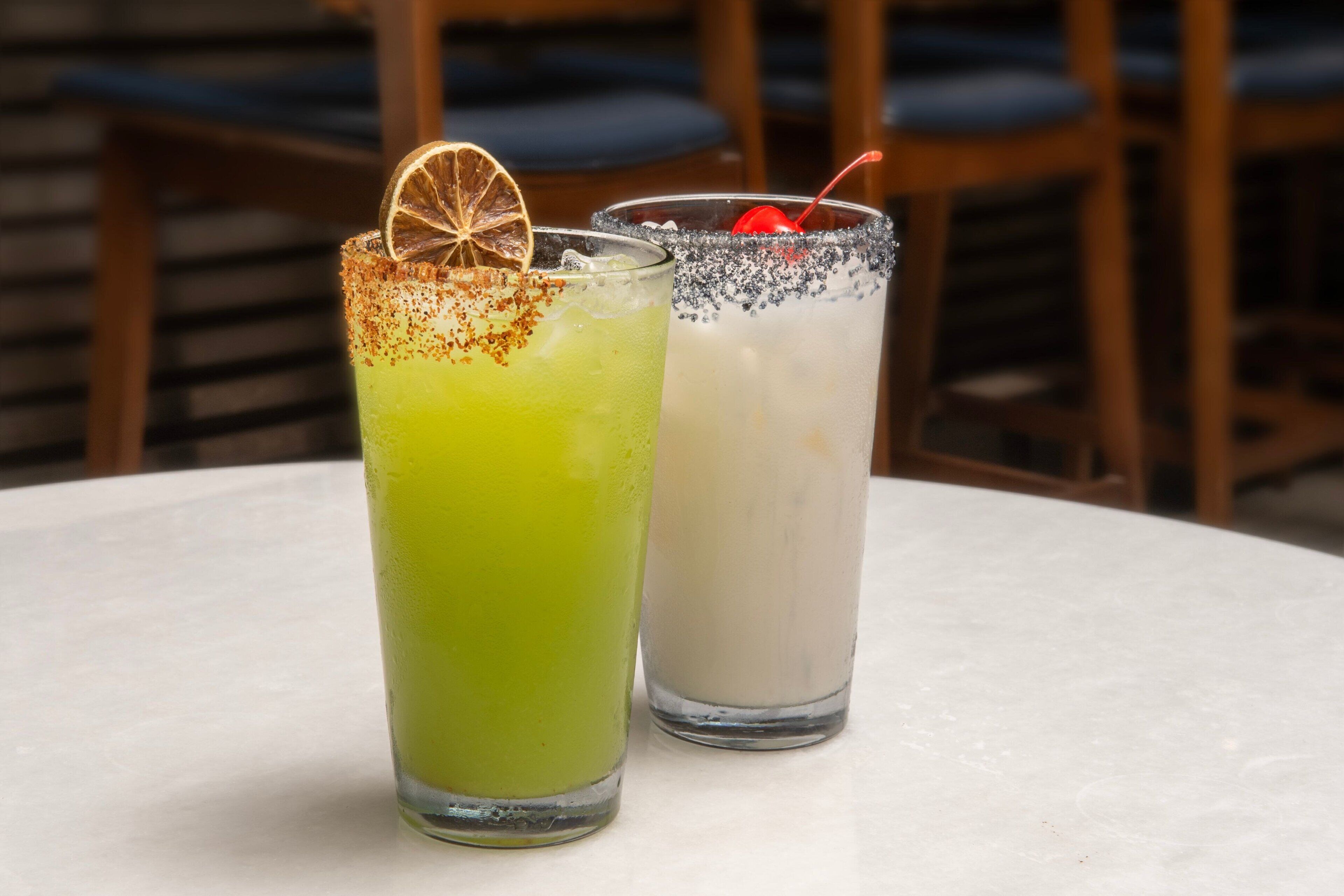Dos bebidas sobre una mesa, con sillas al fondo.