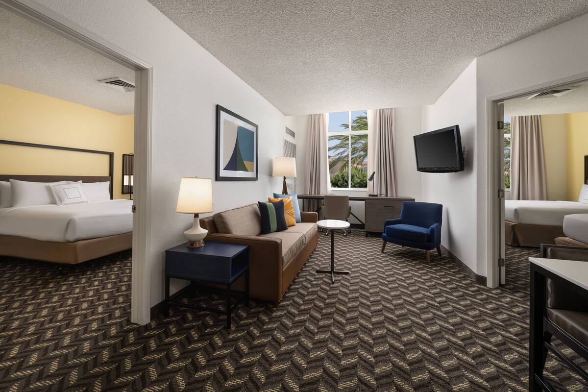 Une chambre d’hôtel avec un lit, un canapé, une chaise, une petite table, un téléviseur et une fenêtre avec des rideaux.