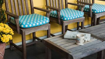 A wooden bench with a polka dot cushion, a wooden table with a mug and newspaper, and a yellow wall in the background.