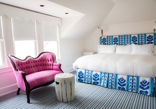 A bedroom with a large bed, a pink armchair, a round side table, and a patterned headboard.