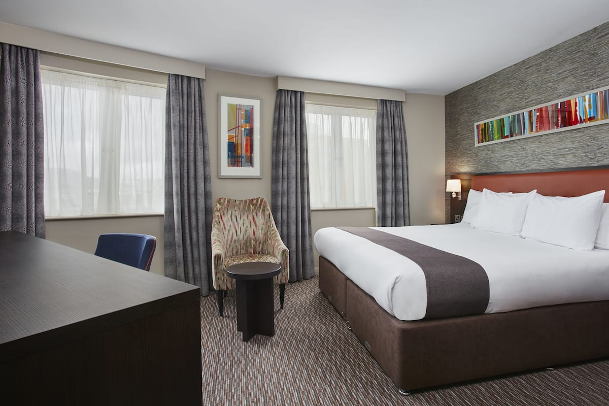 A hotel room with a large bed, a desk, a chair, and a small table.