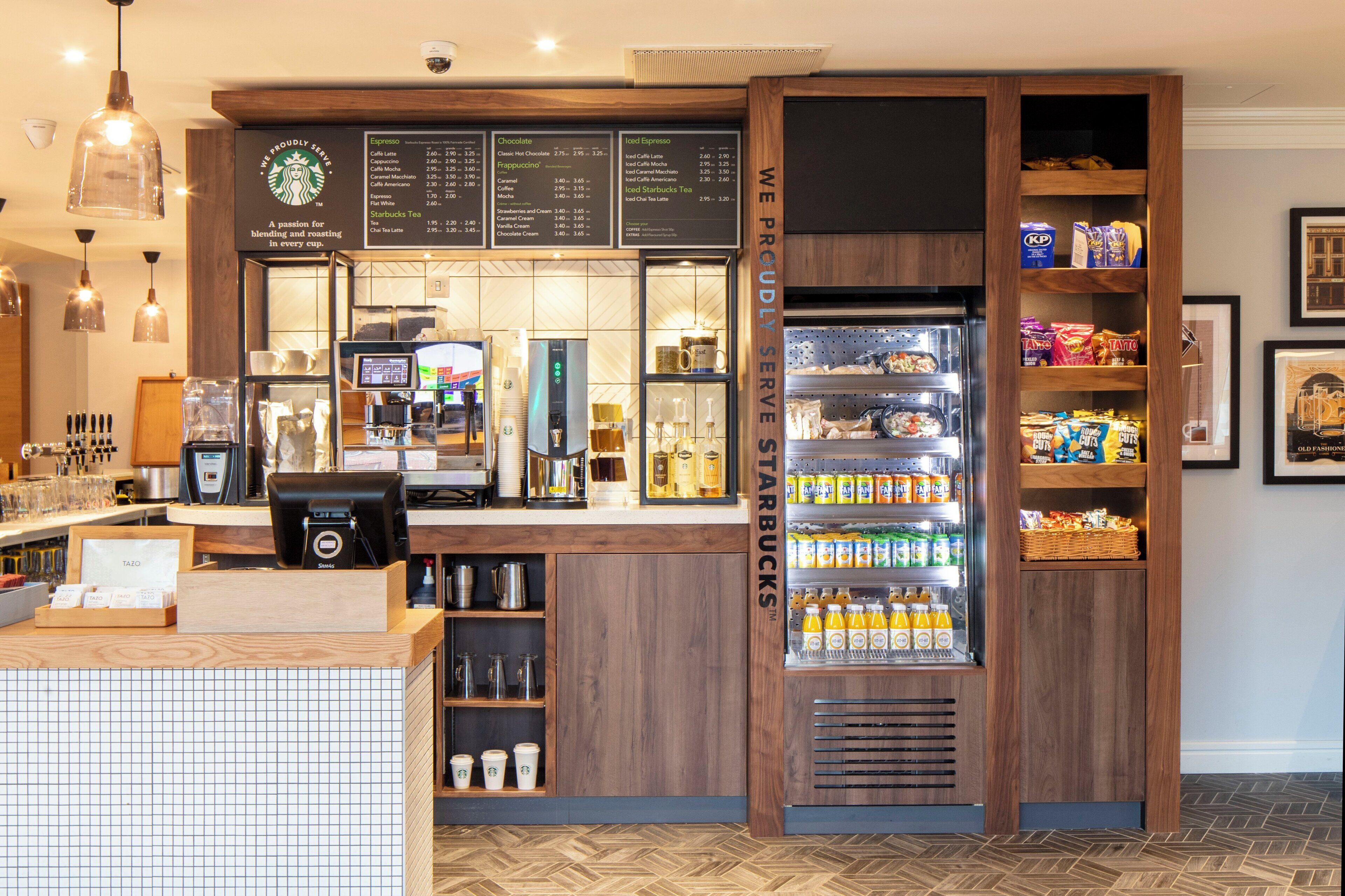 A coffee shop interior with a menu board, espresso machines, a refrigerated display case, and a counter with a coffee grinder.