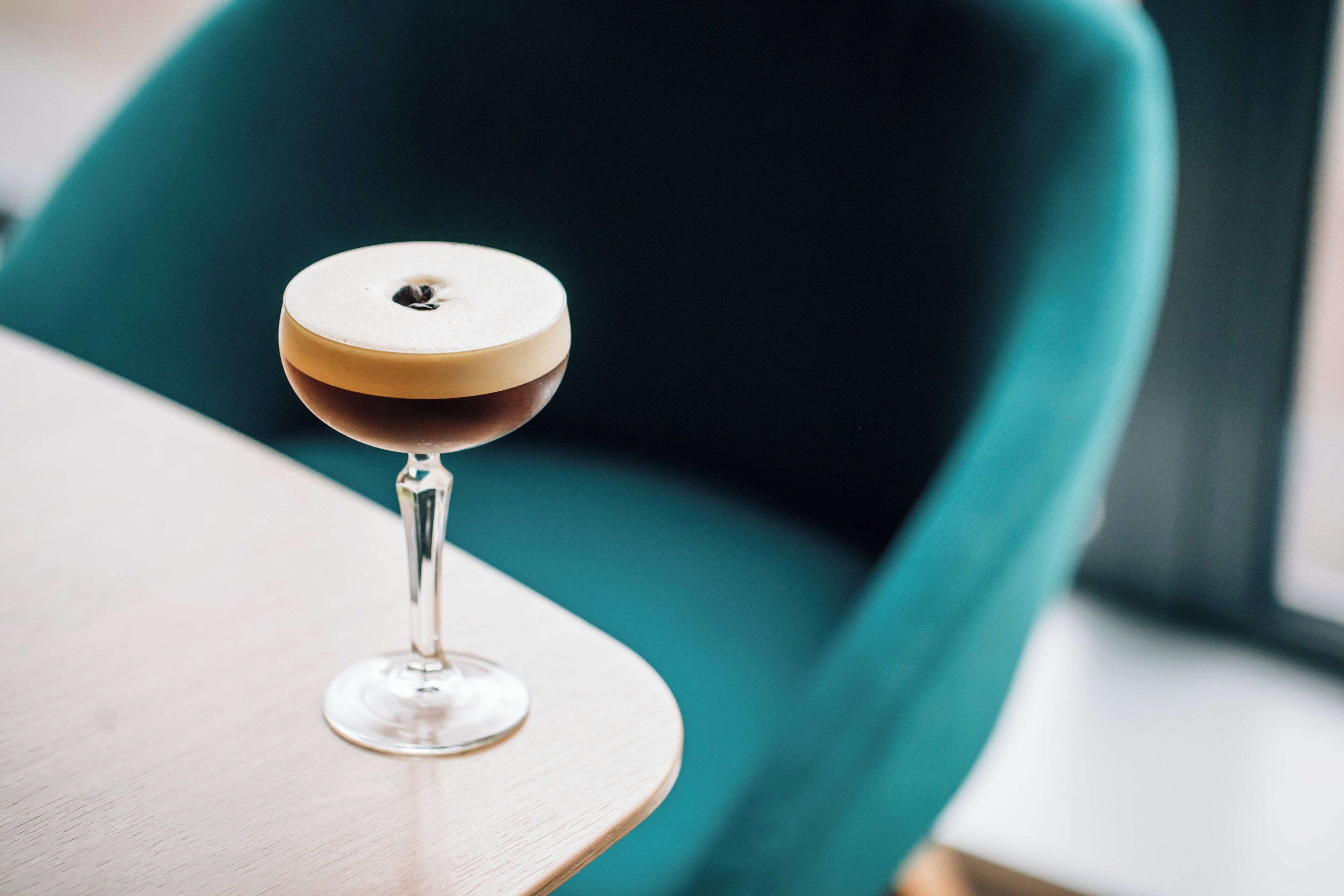 Una copa de martini sobre una mesa de madera, con una silla verde azulada al fondo.