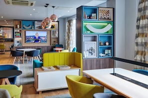 Eine moderne Hotelhalle mit Fernseher, Sitzbereichen und einer Bar.