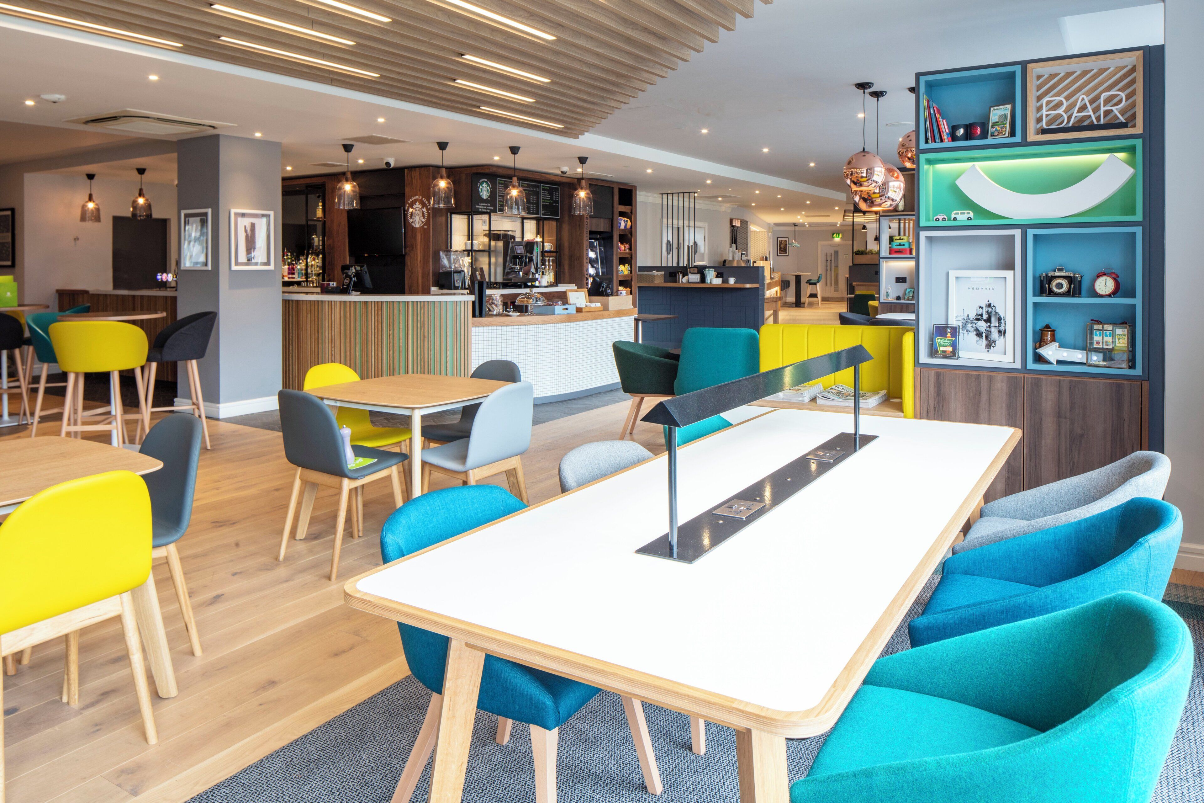 A modern cafe with a bar area, wooden flooring, and colorful chairs.