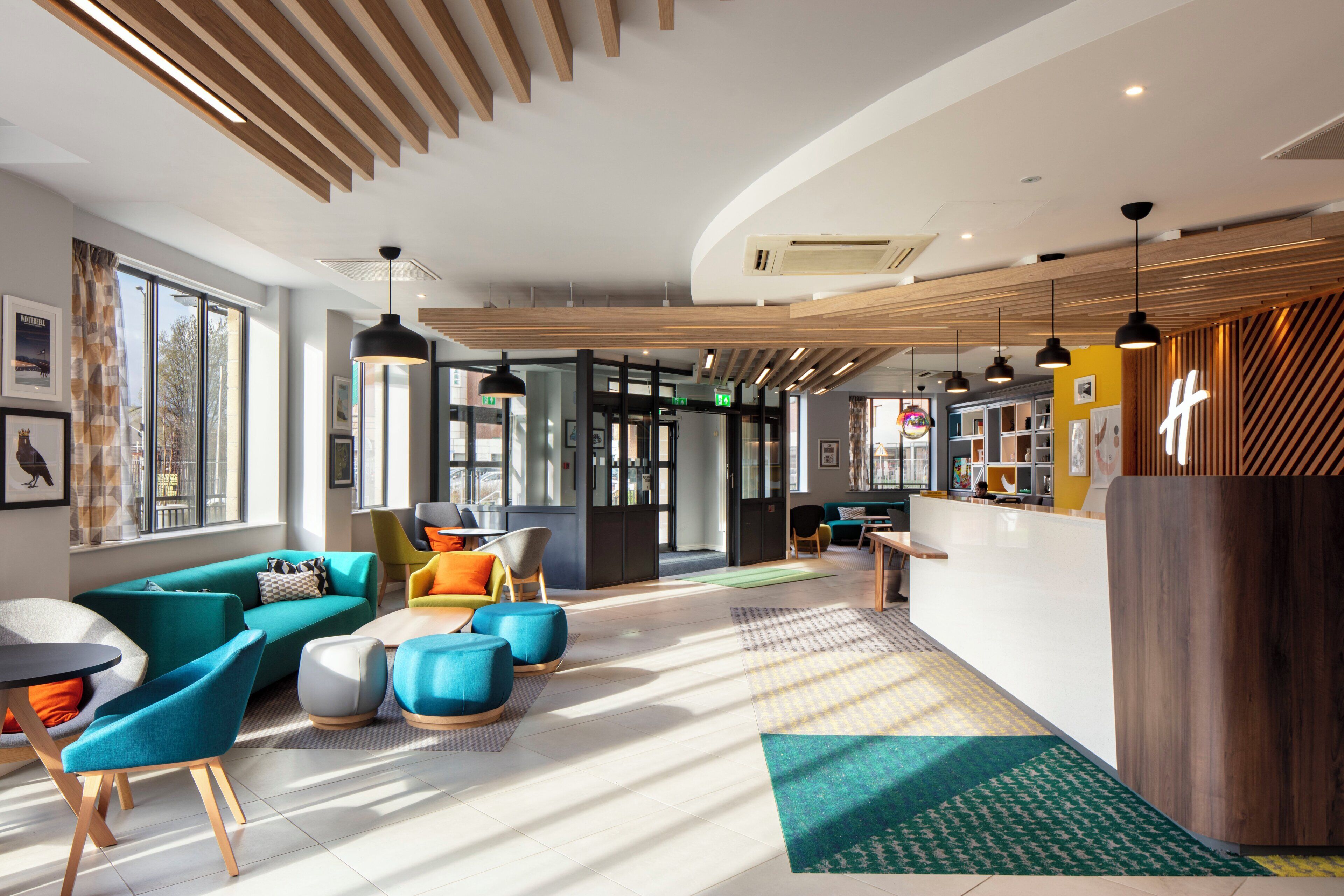 Un intérieur moderne avec un plafond incurvé, un espace salon doté de canapés et de poufs colorés, un comptoir d’accueil et une vue dégagée grâce à de grandes fenêtres.
