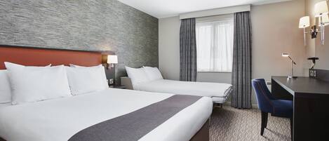 A hotel room with two beds, a desk, and a chair.