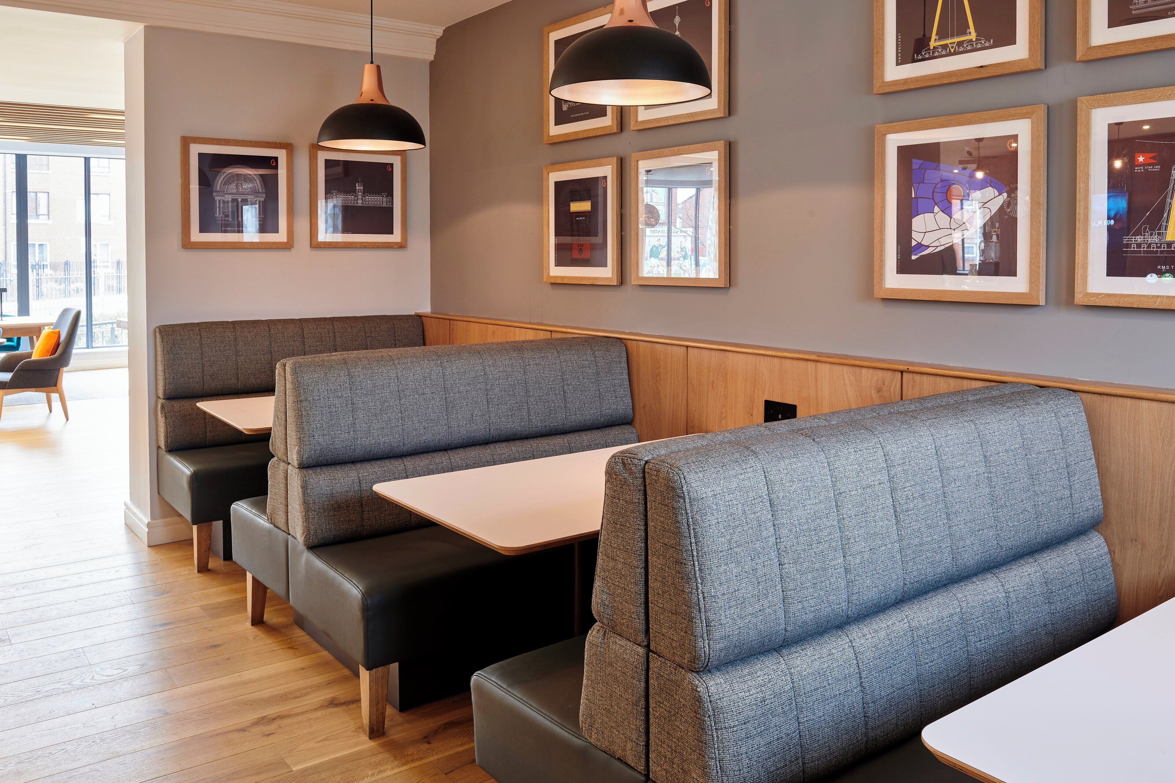 Een restaurantinterieur met ruimtes met zitjes, tafels, hanglampen en kunstwerken in lijsten aan de muren.