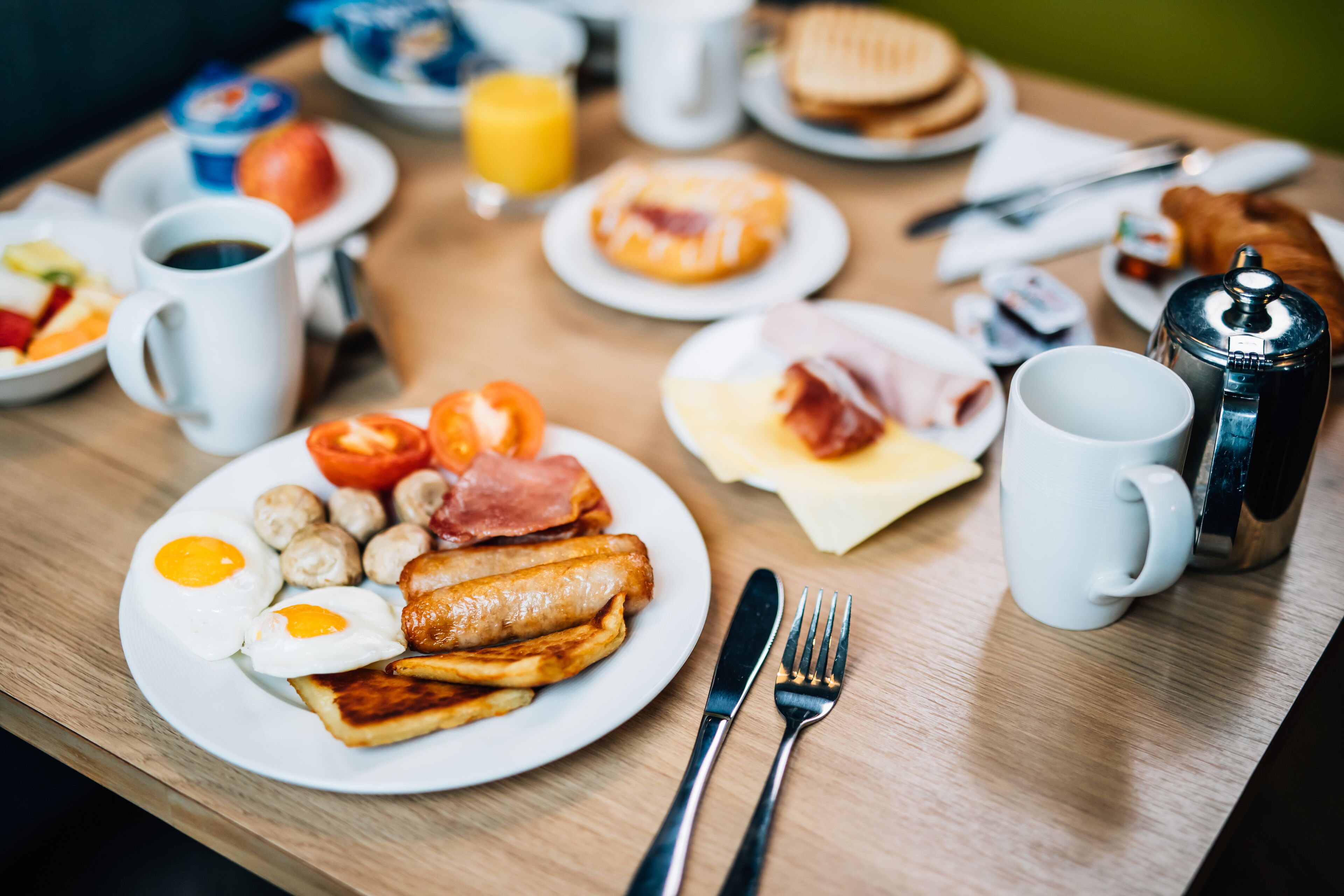 A breakfast table with plates of eggs, sausages, and toast.