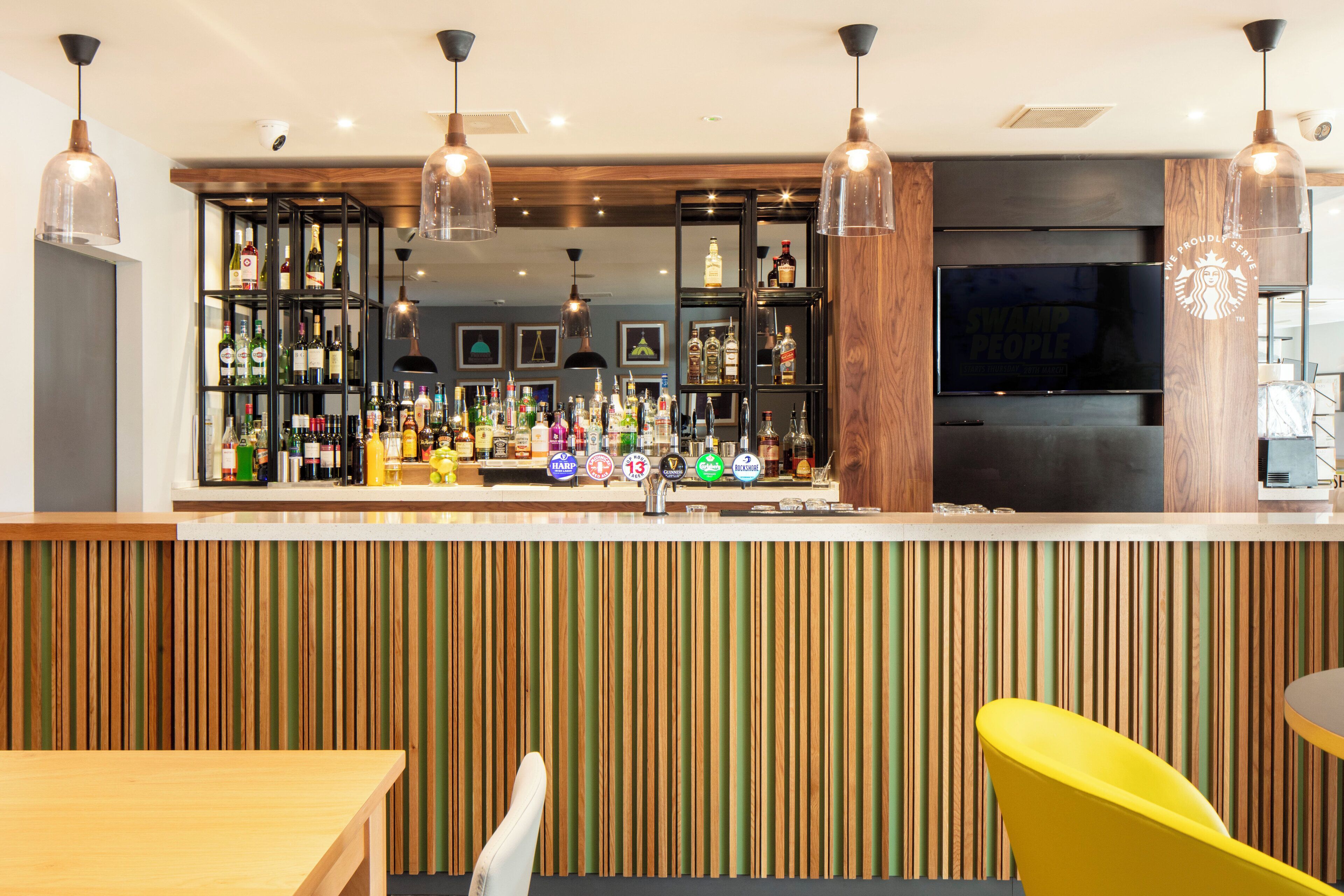 A bar area with a wooden slat wall, multiple liquor bottles, and a television screen.