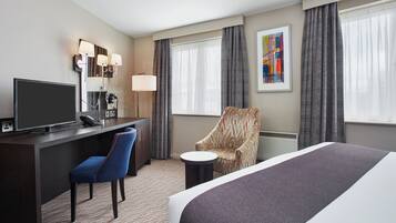 Une chambre d’hôtel avec un lit, un bureau avec une télévision, une chaise, une lampe et un tableau au mur.