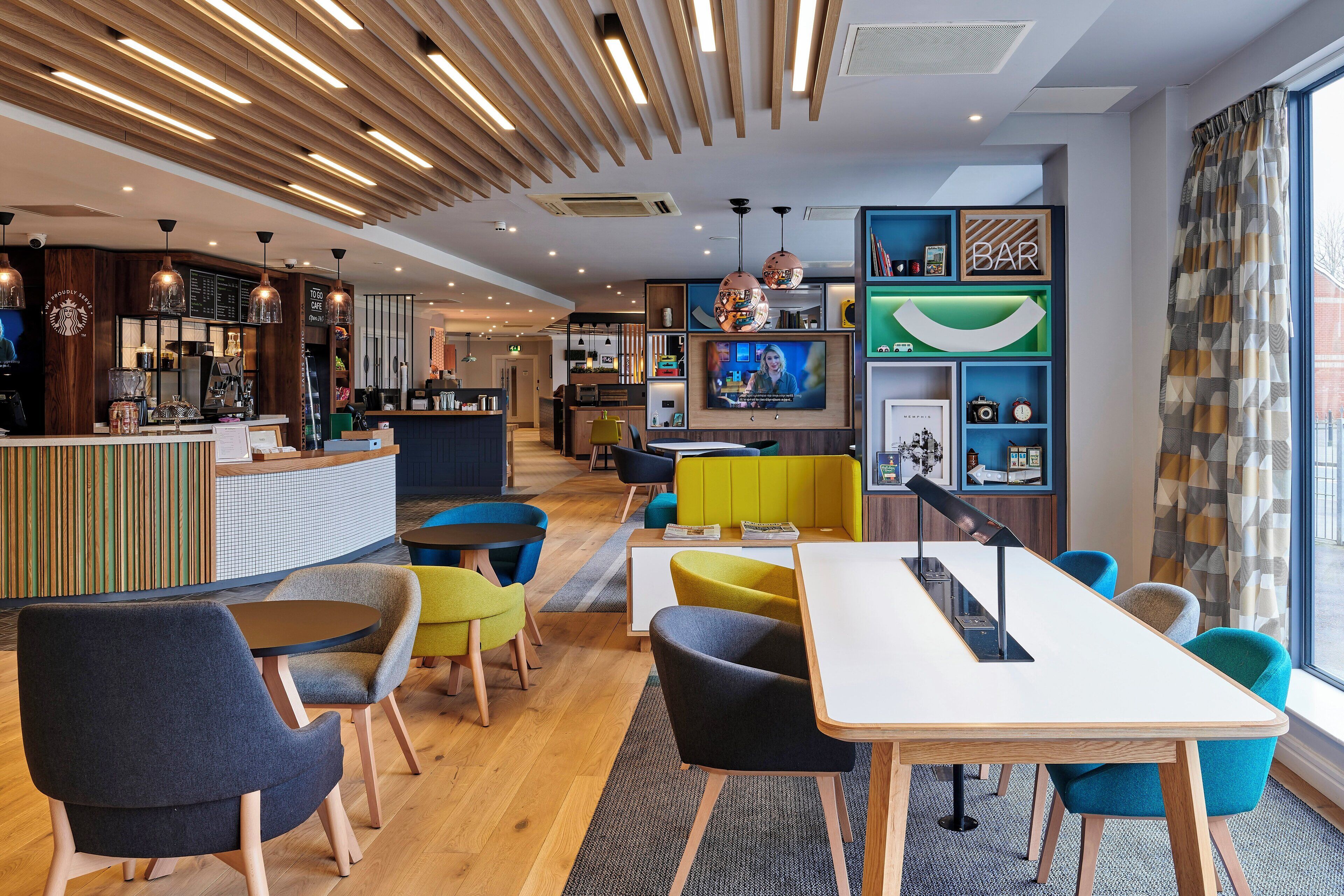 A modern hotel lobby with a bar area, seating arrangements, and a television screen.