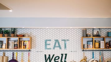 A breakfast bar with a hexagonal tile backsplash, a wooden shelf with kitchen items, and a sign that reads "EAT Well!"